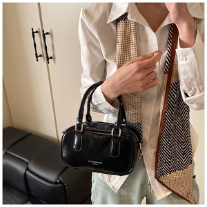 Détail d'un sac à main noir en cuir verni avec double poignée et lettrage de la marque