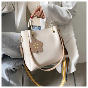 Detail der cremeweißen Beuteltasche mit gestreiftem Gurt und Blumenanhänger