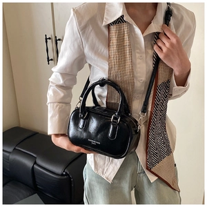 Détail d'un sac à main noir en similicuir brillant avec doubles poignées et boucles en métal