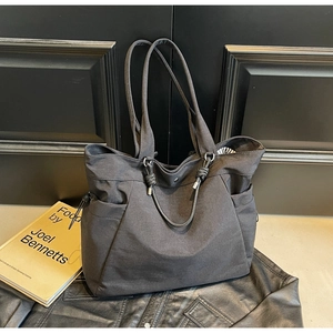 Detail showing high-capacity black fabric tote bag with side pockets and metal hardware