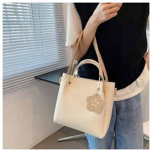 Detail der minimalistischen cremefarbenen Beuteltasche mit Blumenanhänger und Metallgriff