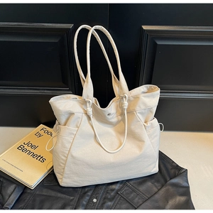 Detailed view of cream canvas tote bag featuring side drawstring and silver metal snap button