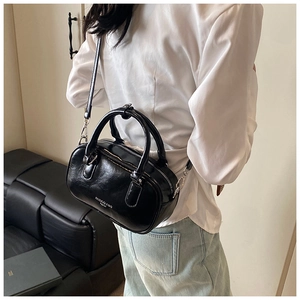 Détail du sac Boston noir brillant avec ferrures argentées porté par un mannequin