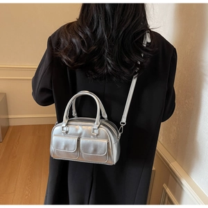 Detail of silver metallic Boston bag featuring dual front pockets and mirror finish texture
