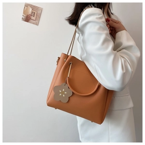 Detail der orange-braunen Beuteltasche mit Blumenanhänger und abnehmbarem Gurt am Modell