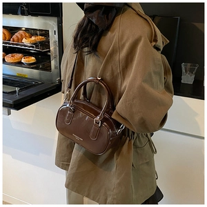 Sac bandoulière chic en cuir marron brillant porté par un mannequin dans une cuisine chaude
