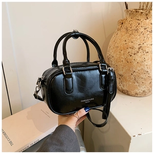 Sac Boston noir brillant avec poignées et bandoulière réglable dans un décor lifestyle