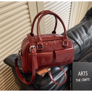 Detail view of deep red oil wax leather Boston bag with two front pockets on leather sofa