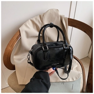 Détail d'un sac Boston noir brillant avec poignées sur un fond de blazer beige