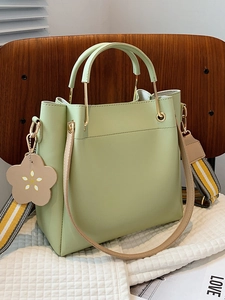 Minimalistische grüne Leder-Beuteltasche mit gestreiftem Gurt auf einem weißen Kissen