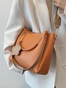 Minimalistische ziegelrote Bucket Bag aus Leder mit gewebtem Gurt auf weißem Blazer