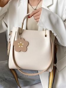 Minimalistische cremefarbene Beuteltasche mit Blumenanhänger und gestreiftem Gurt am Model