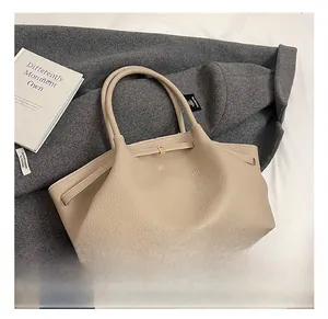 Close-up of beige lychee grain leather tote bag with gold metal buckles on a wool coat