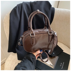 Détail d'un sac Boston en cuir brillant marron foncé sur un fauteuil au style moderne