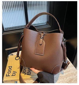 Detailed close-up of brown litchi grain leather bucket bag with white contrast stitching