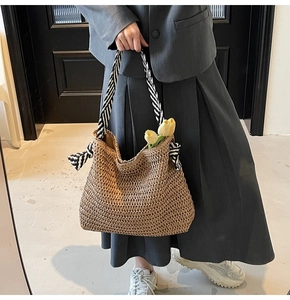 Détail d'un sac cabas en paille tressée avec poignées rayées noir et blanc et nœuds décoratifs