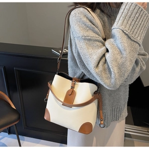 Detail of cream pebbled leather bucket bag with brown accents and gold-tone metal buckle
