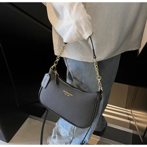 Détail d'un sac sous les bras noir à texture tissée avec chaîne dorée et bandoulière