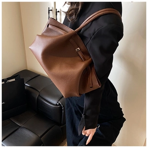 Detail of a brown lychee pattern leather tote bag with thin straps and metal buckle