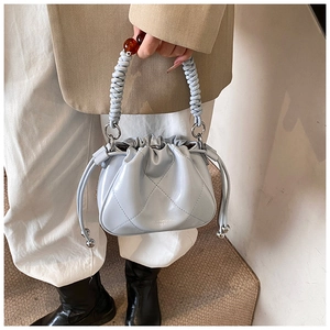 Detail of light blue quilted bucket bag featuring a woven handle and amber bead accent