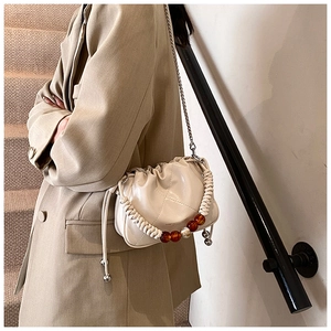 Close-up of pleated cream dumpling bag featuring woven beaded handle and metal chain