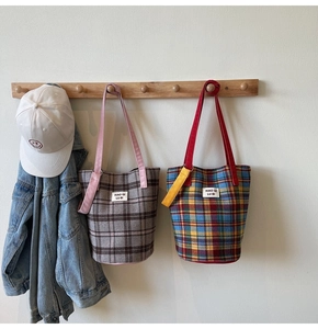 Detail of two plaid canvas tote bags with contrast straps hanging on wooden hooks