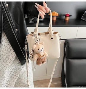 Detail of lychee pattern cream bucket bag featuring rope handles and teddy bear charm