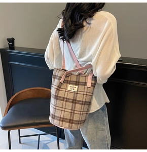 Detail of checkered canvas tote bag with pink contrast handles and brand label on shoulder