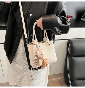 Detail of a creamy white lychee-pattern bucket bag with woven handle and teddy bear charm