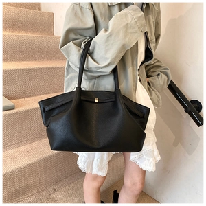 Detail view of large black pleated leather tote bag with gold lock buckle and long straps