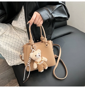 Detail of beige lychee grain leather bucket bag featuring a cute teddy bear charm