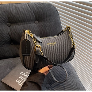 Détail du sac sous l'aisselle à texture tissée noire avec logo doré et bandoulière chaîne