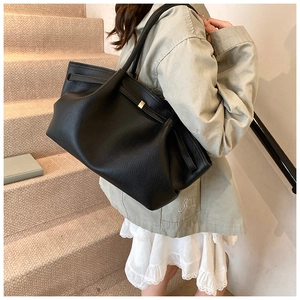 Chic black pleated tote bag in litchi leather shown on a model in a stairwell