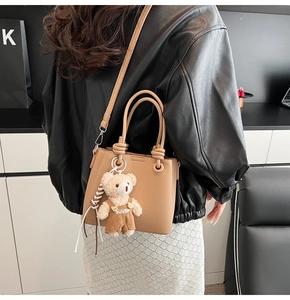 Detail of light brown lychee grain leather bucket bag with a cute plush bear pendant accessory