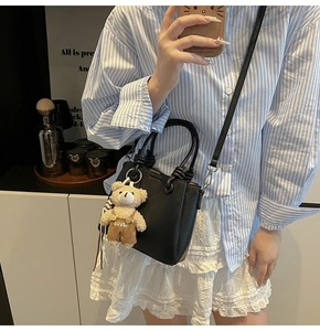 Detailed view of black litchi pattern leather bucket bag with cute plush bear charm