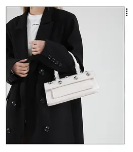 Détail d'un sac baguette en cuir blanc avec clous argentés et poignée supérieure fixe
