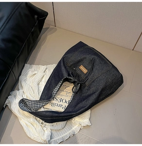 Détail du cabas en denim bleu avec bretelles à carreaux et écusson logo en cuir brun