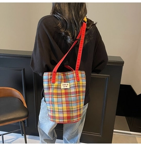 Detail view of colorful plaid tote bag with red handles and woven fabric texture