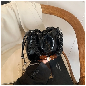 Detail of black glossy bucket bag featuring marble resin beads and silver chain strap