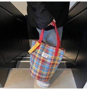 Detail of colorful plaid tote bag with red handles and brand label on steps