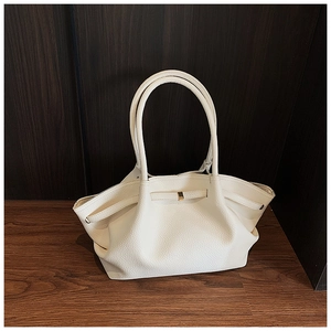 Close-up of cream textured leather tote bag with gold metal buckle on wooden surface
