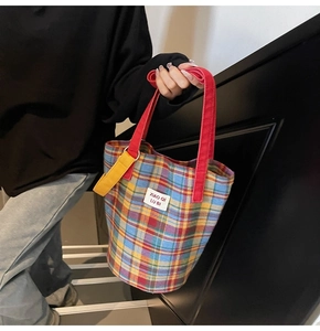 Detailed close-up of a colorful plaid tote bag made of woven tweed fabric with red handles