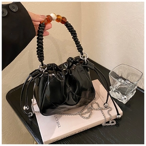 Detail of black quilted bucket bag with amber beaded handle and silver chain strap