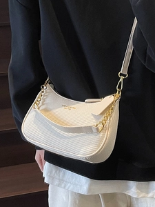 Sac hobo beige tissé minimaliste avec chaîne dorée porté par un mannequin en tenue noire