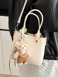 Minimalist creamy white lychee grain bucket bag with unique knot handle and teddy bear charm