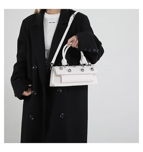 Détail du sac baguette en cuir verni blanc avec rivets argentés sur un blazer noir