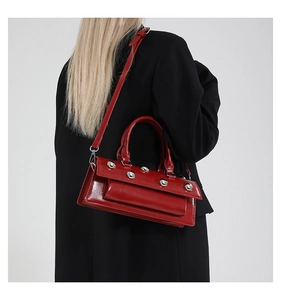 Détail du sac baguette en cuir verni rouge avec cinq gros clous ronds en métal argenté
