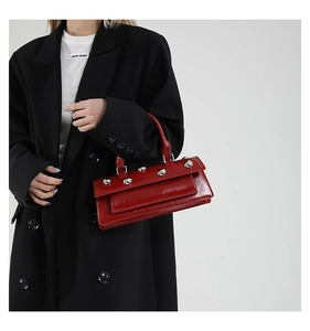 Détail du sac bandoulière en cuir brillant rouge foncé avec clous argentés sur un mannequin