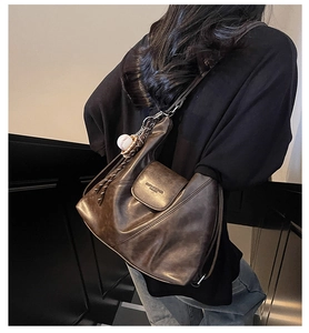 Detail of dark brown leather tote bag with Kindlybear logo and white ball charm on back