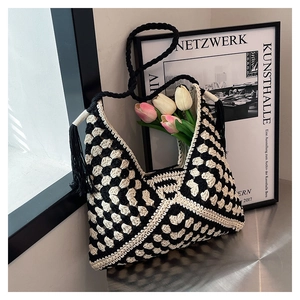 Detailed close-up of hand-knitted checkerboard crochet bag with black tassel and long braided strap